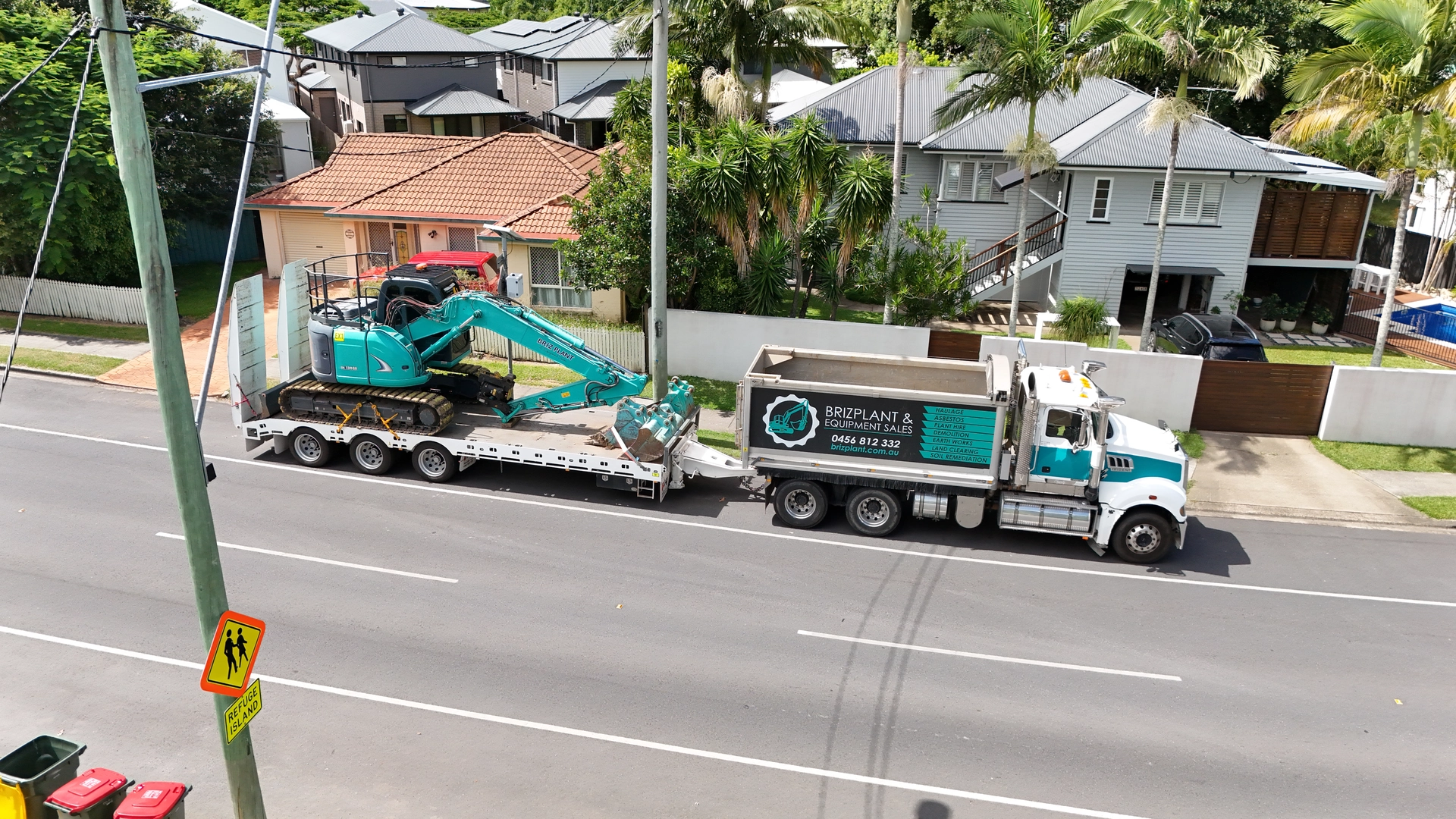 Float haulage truck transporting 14 ton excavator through residential Brisbane street